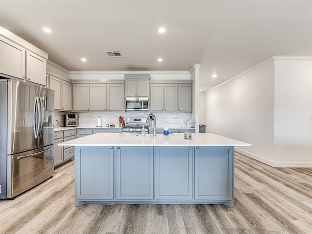 kitchen with stainless steel appliances, an island with sink, light countertops, and visible vents