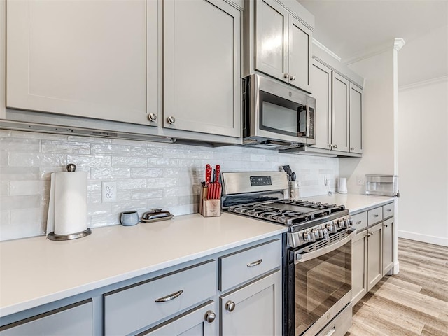 kitchen featuring gray cabinetry, stainless steel appliances, light countertops, backsplash, and crown molding