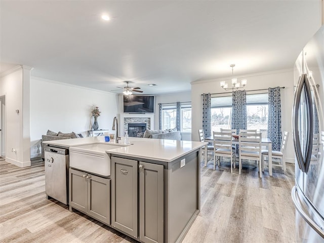 kitchen featuring open floor plan, a kitchen island with sink, gray cabinets, stainless steel appliances, and light countertops