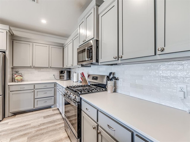 kitchen with tasteful backsplash, gray cabinets, light countertops, appliances with stainless steel finishes, and light wood-type flooring