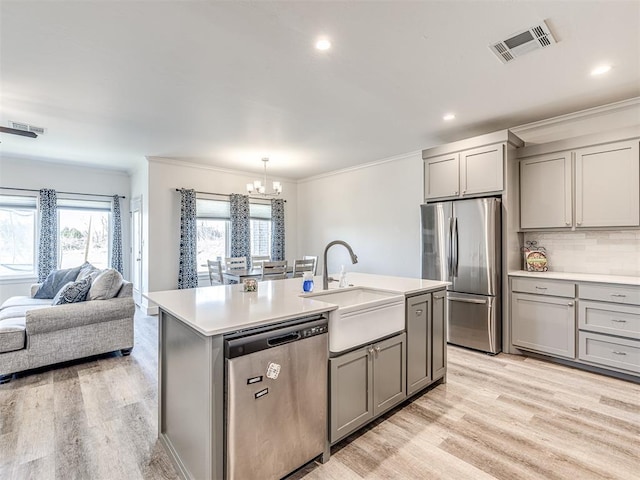 kitchen with visible vents, a kitchen island with sink, stainless steel appliances, light countertops, and a sink