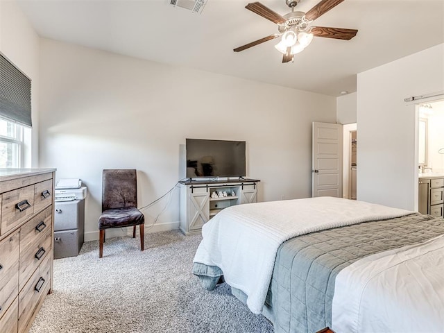 bedroom featuring ceiling fan, light colored carpet, visible vents, baseboards, and ensuite bath