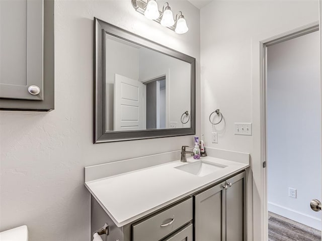 half bathroom featuring vanity, baseboards, and wood finished floors