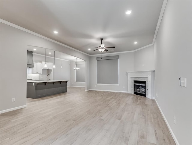 unfurnished living room featuring ceiling fan with notable chandelier, a sink, a high end fireplace, baseboards, and light wood-style floors