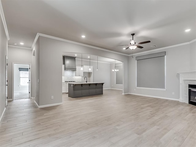 unfurnished living room with light wood-type flooring, a fireplace, a sink, and ceiling fan with notable chandelier
