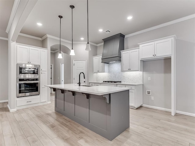 kitchen featuring premium range hood, a sink, light countertops, appliances with stainless steel finishes, and hanging light fixtures
