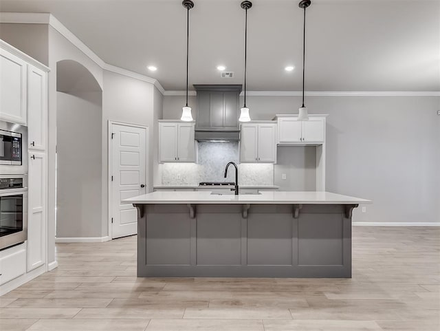 kitchen with arched walkways, decorative light fixtures, a center island with sink, stainless steel appliances, and light countertops
