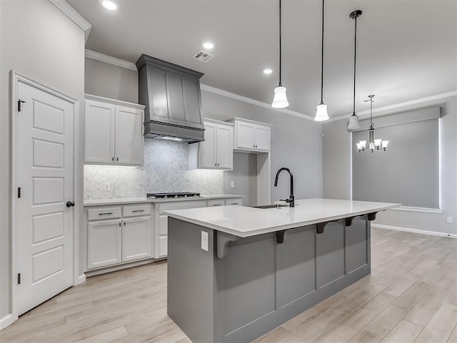 kitchen with an island with sink, light countertops, a sink, and hanging light fixtures