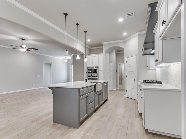 kitchen with arched walkways, light countertops, a center island with sink, and visible vents