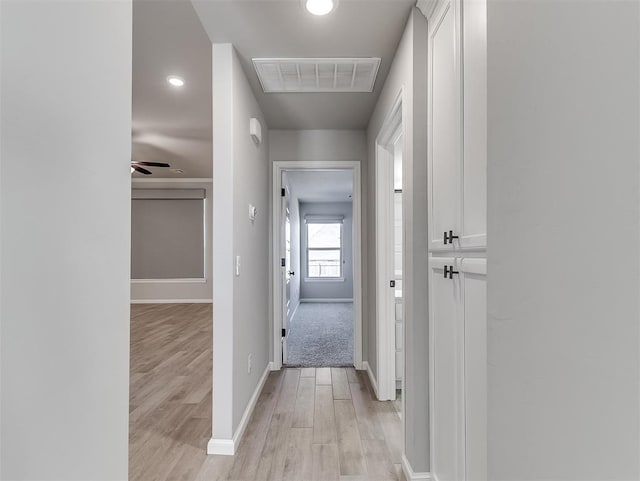 corridor with light wood finished floors, visible vents, and baseboards