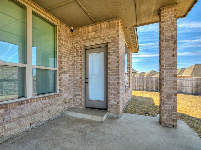 entrance to property featuring a patio area, brick siding, and fence
