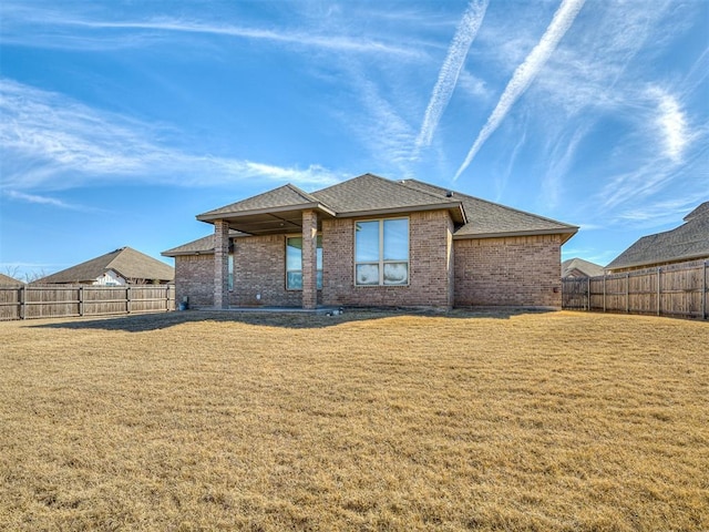 back of house featuring a fenced backyard, roof with shingles, a lawn, and brick siding