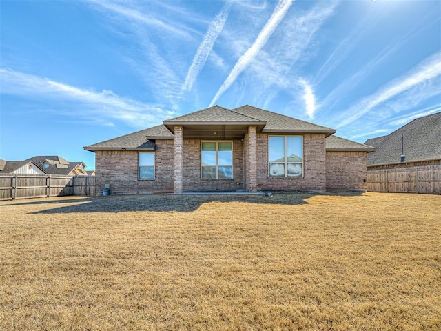 back of property featuring a fenced backyard, roof with shingles, a lawn, and brick siding
