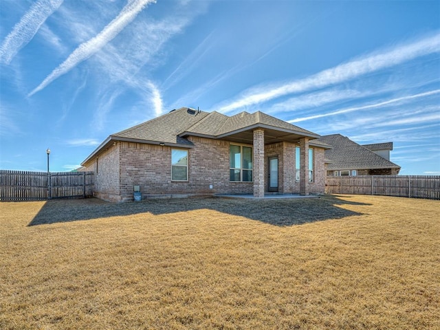back of house featuring a fenced backyard, a yard, brick siding, and roof with shingles