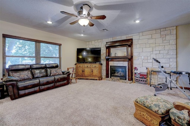 living area with a textured ceiling, a large fireplace, ceiling fan, and carpet