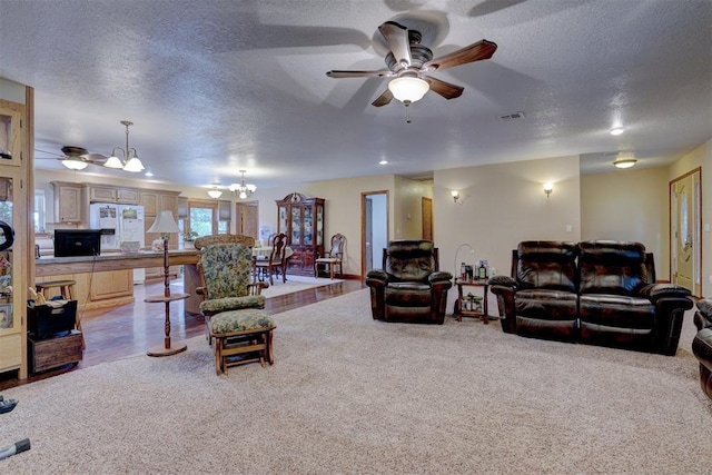 living room featuring a textured ceiling, carpet floors, ceiling fan with notable chandelier, and visible vents