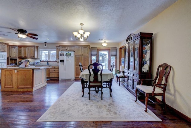 dining space with a textured ceiling, dark wood-style flooring, ceiling fan with notable chandelier, and baseboards