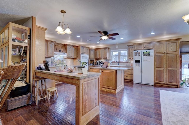 kitchen with a peninsula, white appliances, dark wood-type flooring, and under cabinet range hood