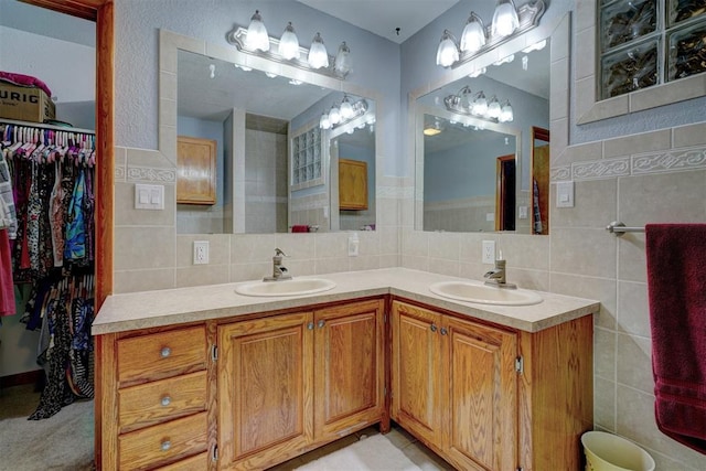 bathroom featuring double vanity, a spacious closet, a sink, and tile walls