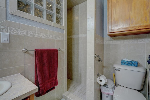 bathroom with toilet, tiled shower, a sink, and tile walls