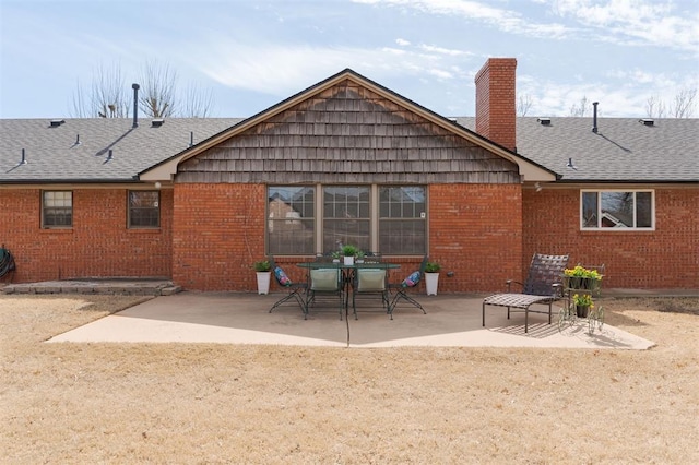 rear view of house featuring brick siding, a patio, a chimney, and roof with shingles