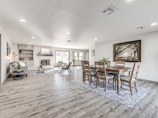 dining area featuring a textured ceiling, a fireplace, visible vents, and light wood-style floors