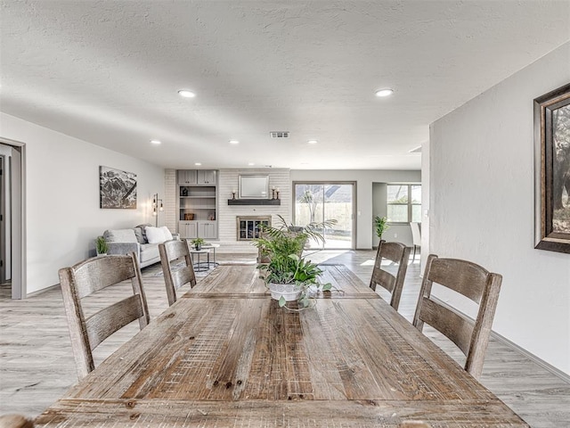 dining room with visible vents, a textured ceiling, light wood-type flooring, a fireplace, and recessed lighting