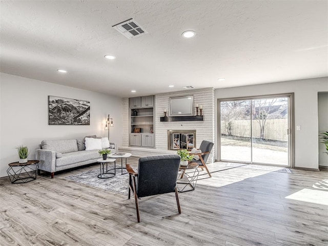 living room featuring visible vents, wood finished floors, a textured ceiling, a brick fireplace, and recessed lighting