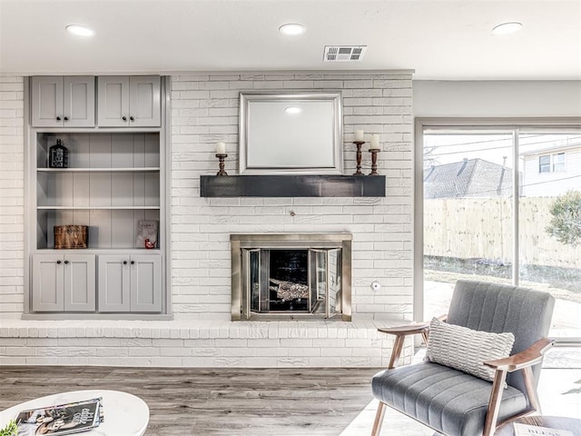 living area with a brick fireplace, wood finished floors, visible vents, and recessed lighting