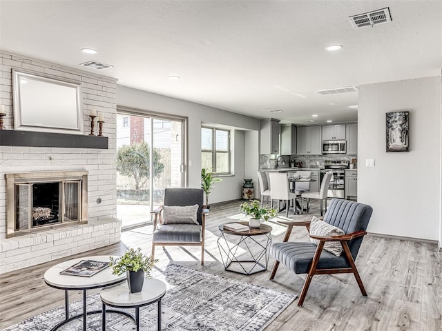 living area featuring light wood-type flooring, visible vents, and a fireplace