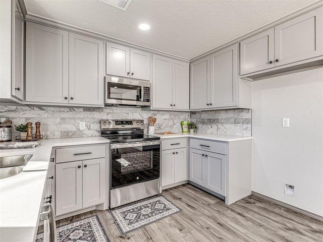 kitchen with stainless steel appliances, light wood-type flooring, gray cabinets, and light countertops