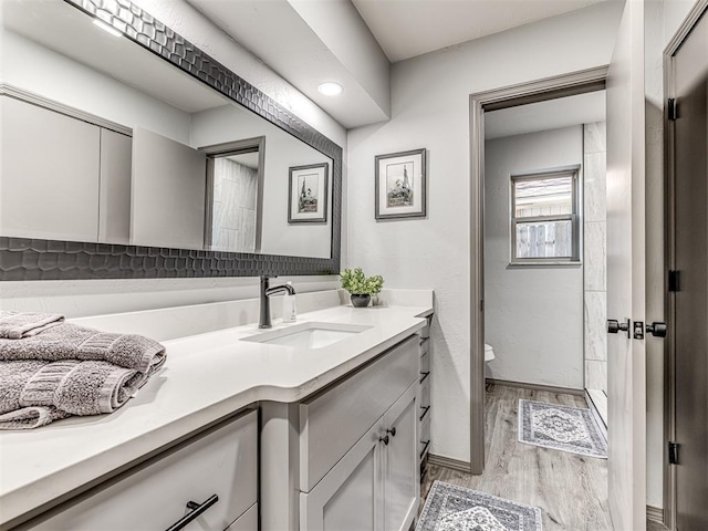 full bath featuring baseboards, toilet, wood finished floors, walk in shower, and vanity