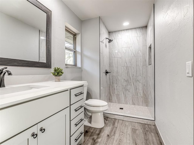 full bathroom featuring a tile shower, vanity, toilet, and wood finished floors