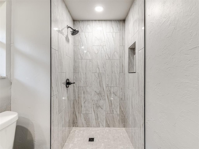 bathroom featuring a textured wall, a tile shower, and toilet