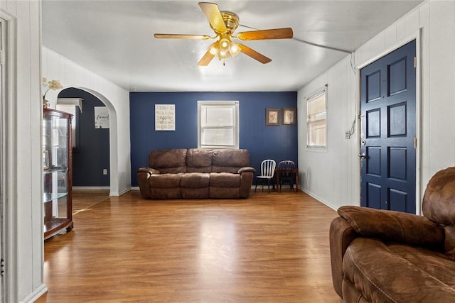 living area with arched walkways, baseboards, light wood-style flooring, and a ceiling fan