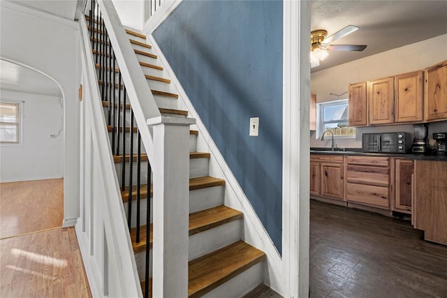 staircase featuring ceiling fan, arched walkways, and wood finished floors