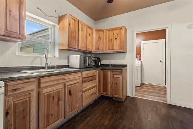 kitchen featuring washer / dryer, dark countertops, a sink, and dark wood-style floors