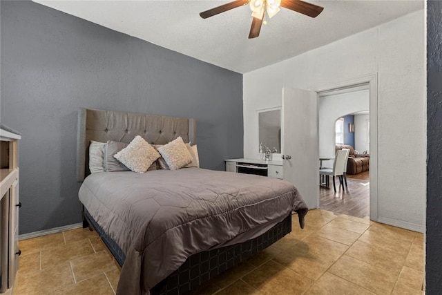 bedroom featuring arched walkways, a ceiling fan, and a textured wall