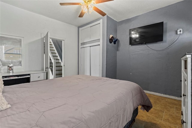 bedroom with baseboards, a ceiling fan, a textured wall, a textured ceiling, and a closet