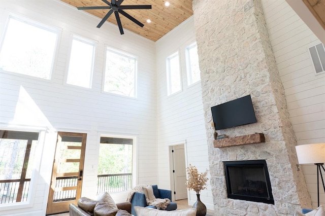 living room featuring plenty of natural light, a stone fireplace, wooden ceiling, and a high ceiling