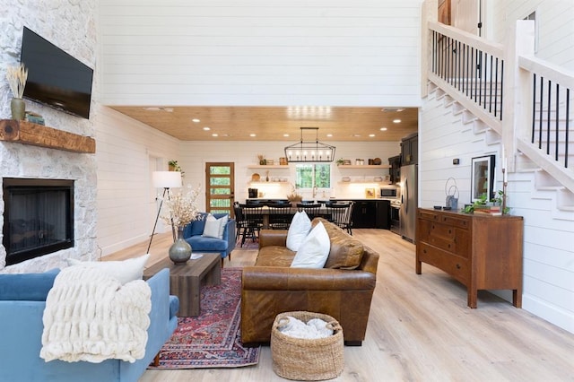 living room featuring wooden walls, stairway, a high ceiling, a stone fireplace, and light wood-type flooring