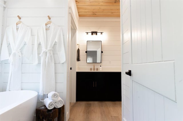 bathroom featuring wood ceiling, wooden walls, vanity, wood finished floors, and a freestanding tub