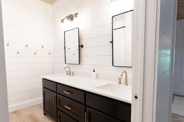 full bath featuring double vanity, wooden walls, a sink, and wood finished floors