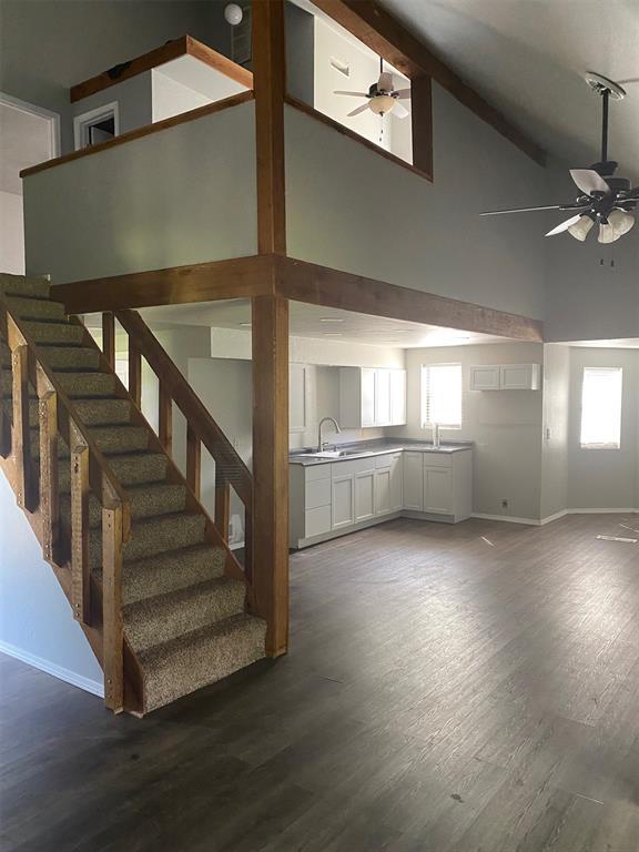 unfurnished living room with ceiling fan, stairway, and dark wood-type flooring