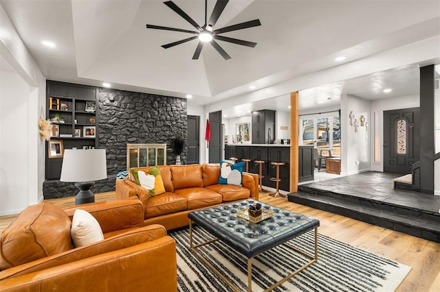 living area featuring built in shelves, a fireplace, ceiling fan, wood finished floors, and baseboards