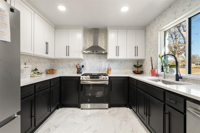 kitchen featuring wall chimney exhaust hood, appliances with stainless steel finishes, a sink, and white cabinets