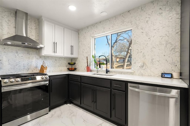 kitchen featuring stainless steel appliances, a sink, white cabinetry, marble finish floor, and wall chimney exhaust hood