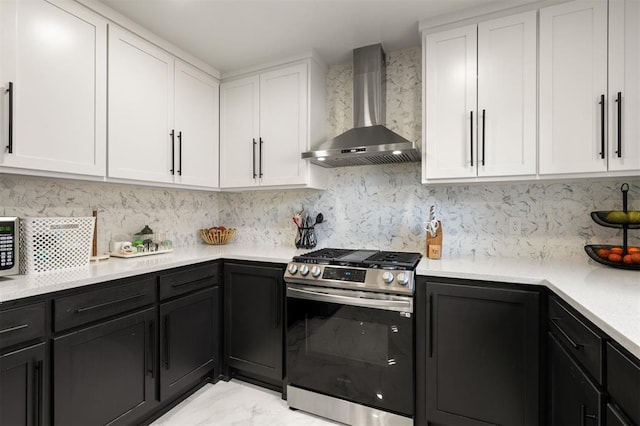 kitchen featuring stainless steel gas range, light countertops, white cabinetry, and wall chimney exhaust hood