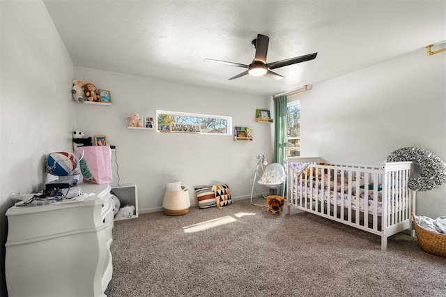 bedroom featuring carpet floors, a nursery area, baseboards, and a ceiling fan