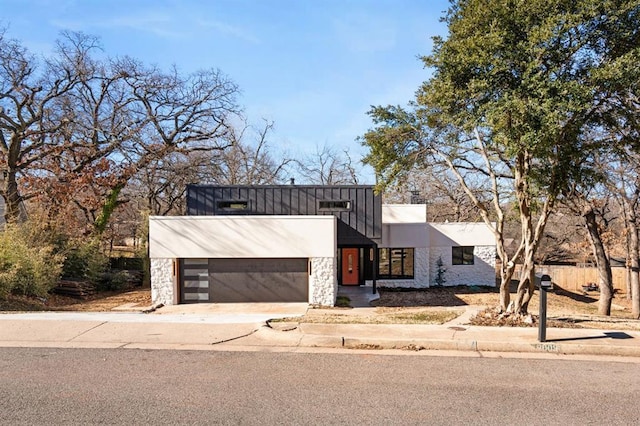 contemporary home with a garage, stone siding, board and batten siding, and driveway